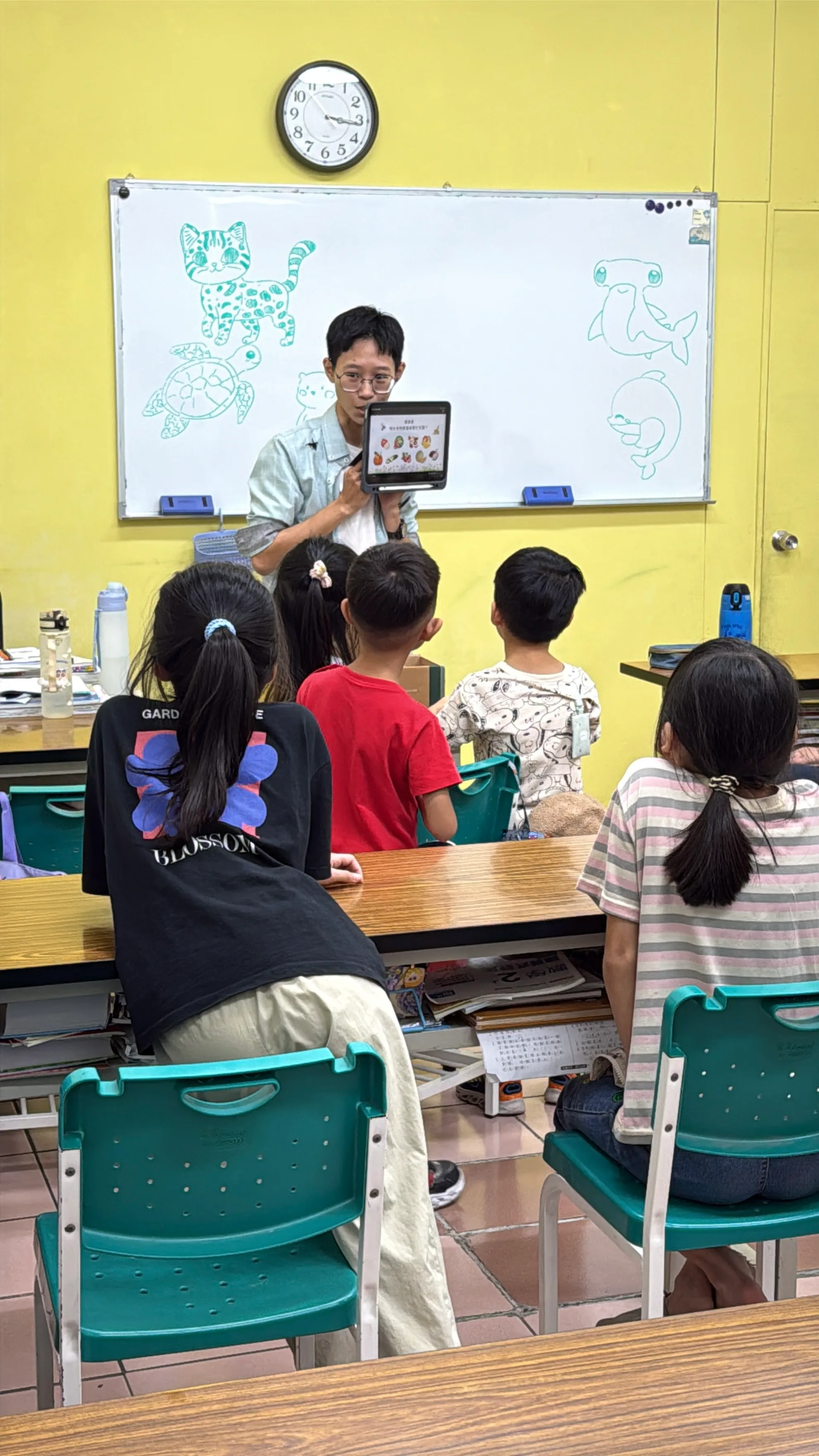 男老師在白板前拿著平板講解,孩子們坐著聽